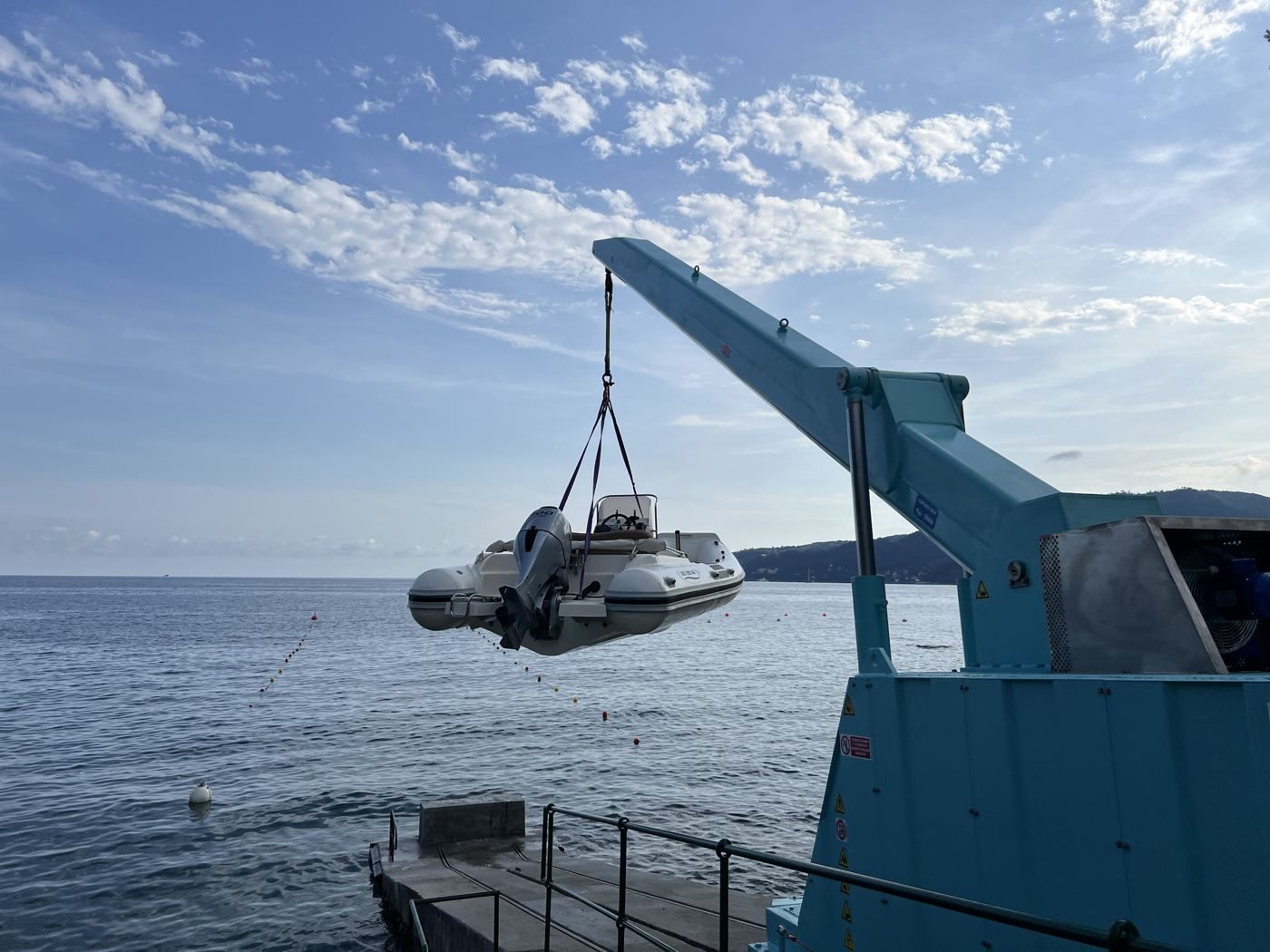 Il bigo solleva un gommone sopra lo scivolo, con il mare e la costa sullo sfondo